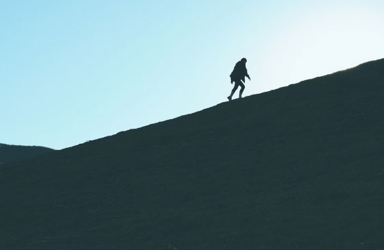 Silhouetted person climbing up a steep slope